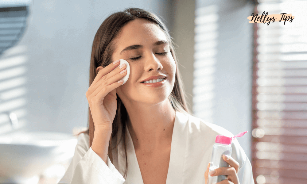 Kvinde i badekåbe renser ansigt med vatrondel og micellar vand, smilende med lukkede øjne.