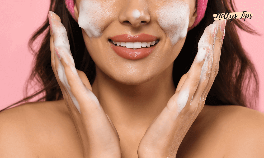 Kvinde med skum i ansigtet og pink baggrund smiler, mens hun renser huden.