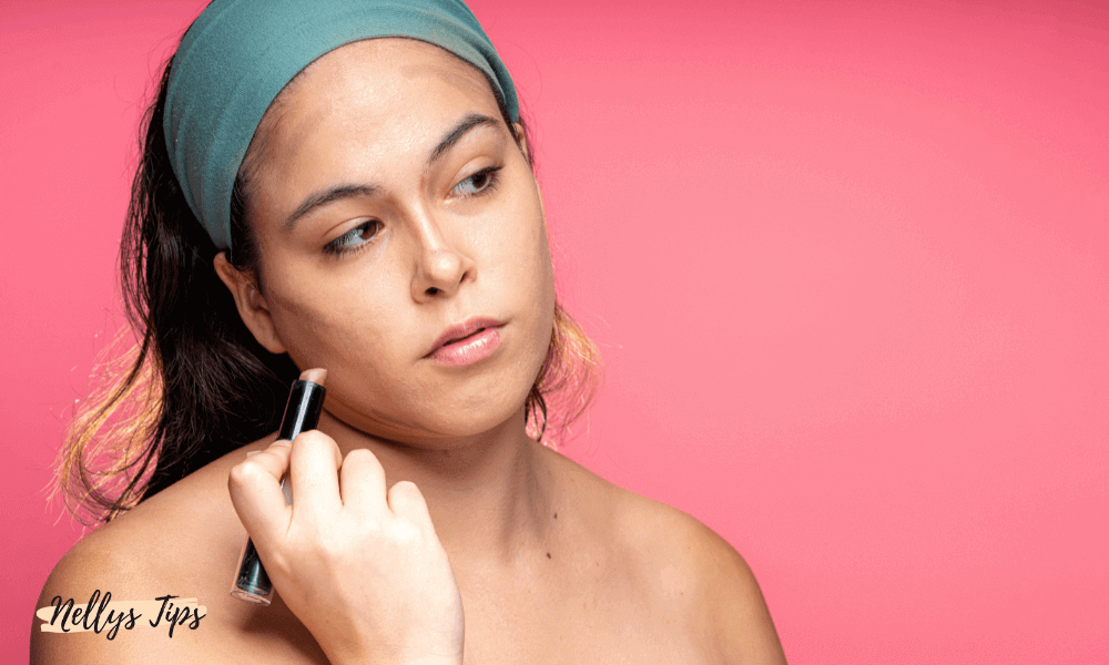 Kvinde påfører contour stick i ansigtet foran pink baggrund med fokus på kindben